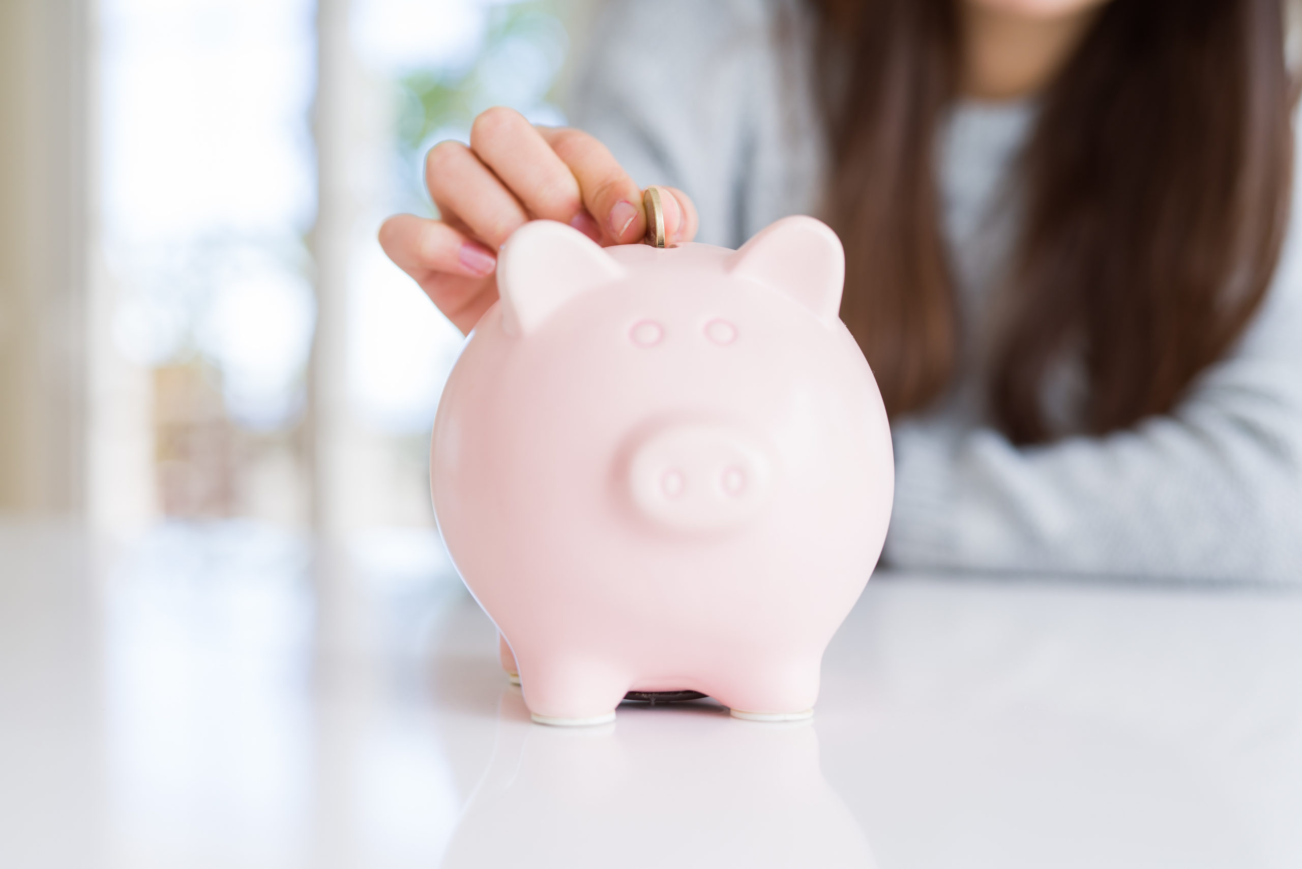 Young woman putting a coin inside piggy bank as savings for investment