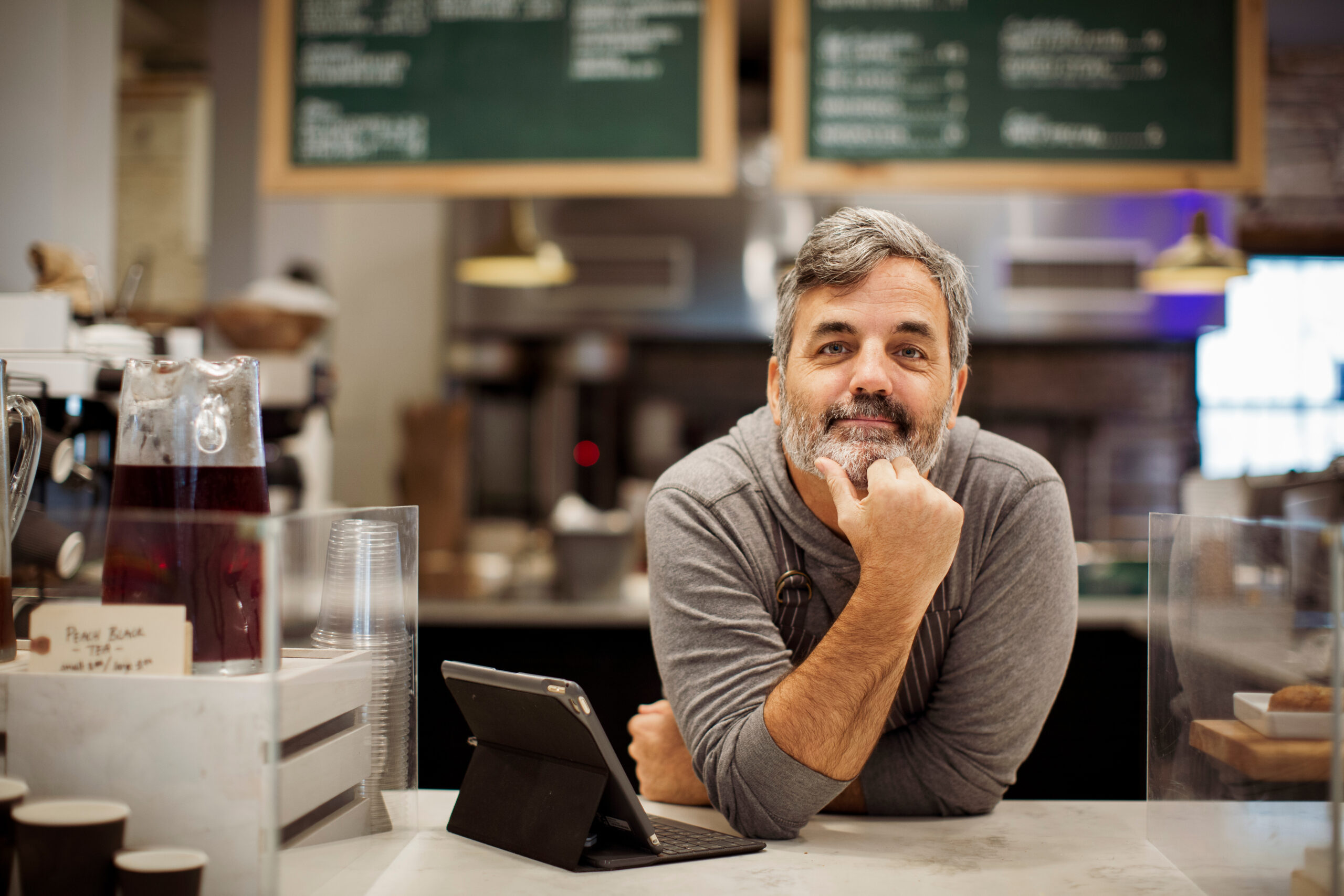 Portrait of owner with tablet computer leaning on counter in caf